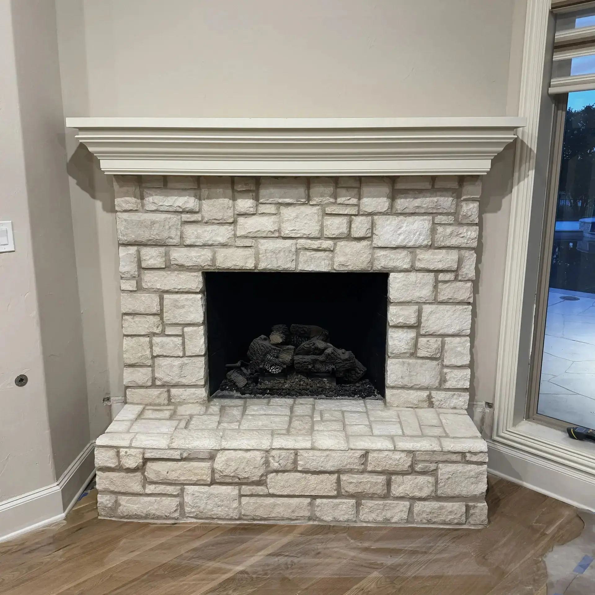 The same offwhite painted corner with a remodeled fireplace made of larger stones, a larger base of the same stone, and a cleaner, more squared design.