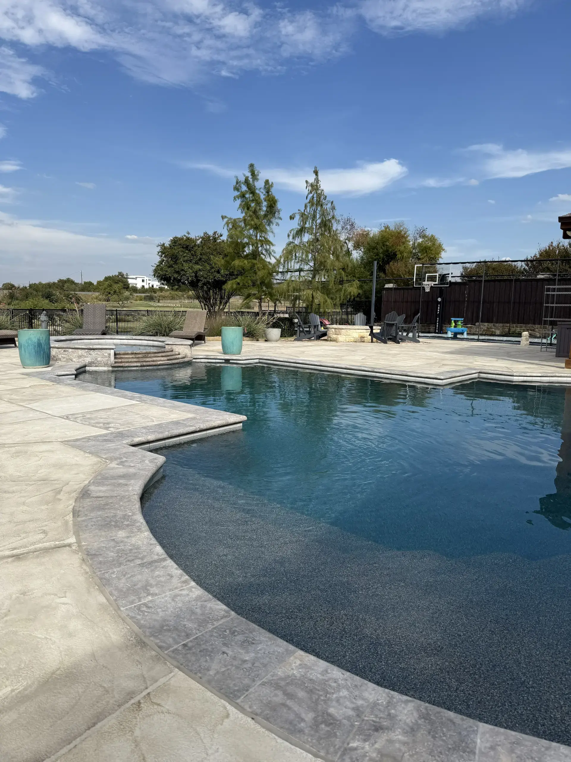 Large blue pool set in a large concrete-covered backyard against a blue sky taken from a diagonal angle