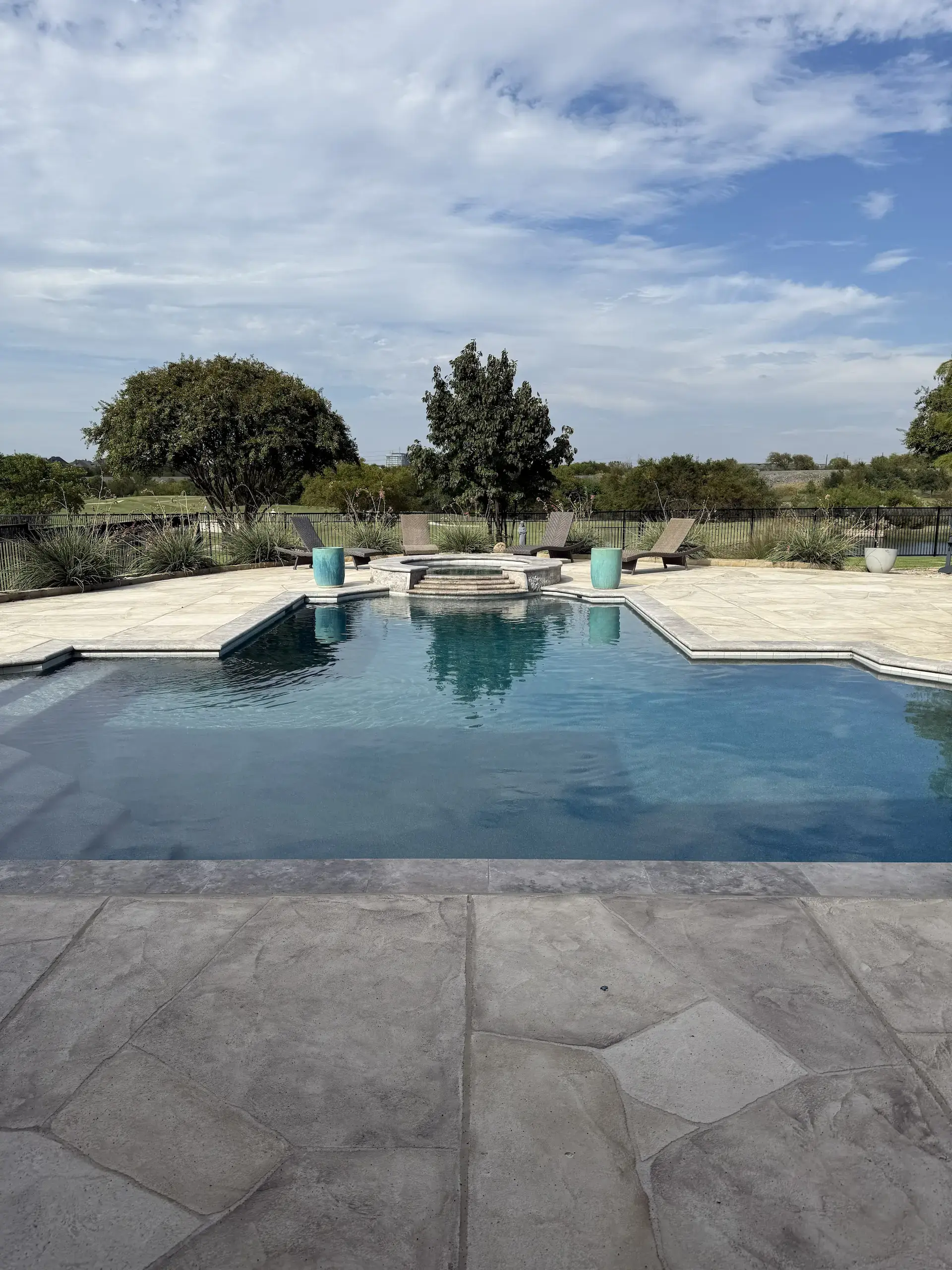 Large blue pool in a concrete backyard against a blue sky taken from a straight, symmetrical angle