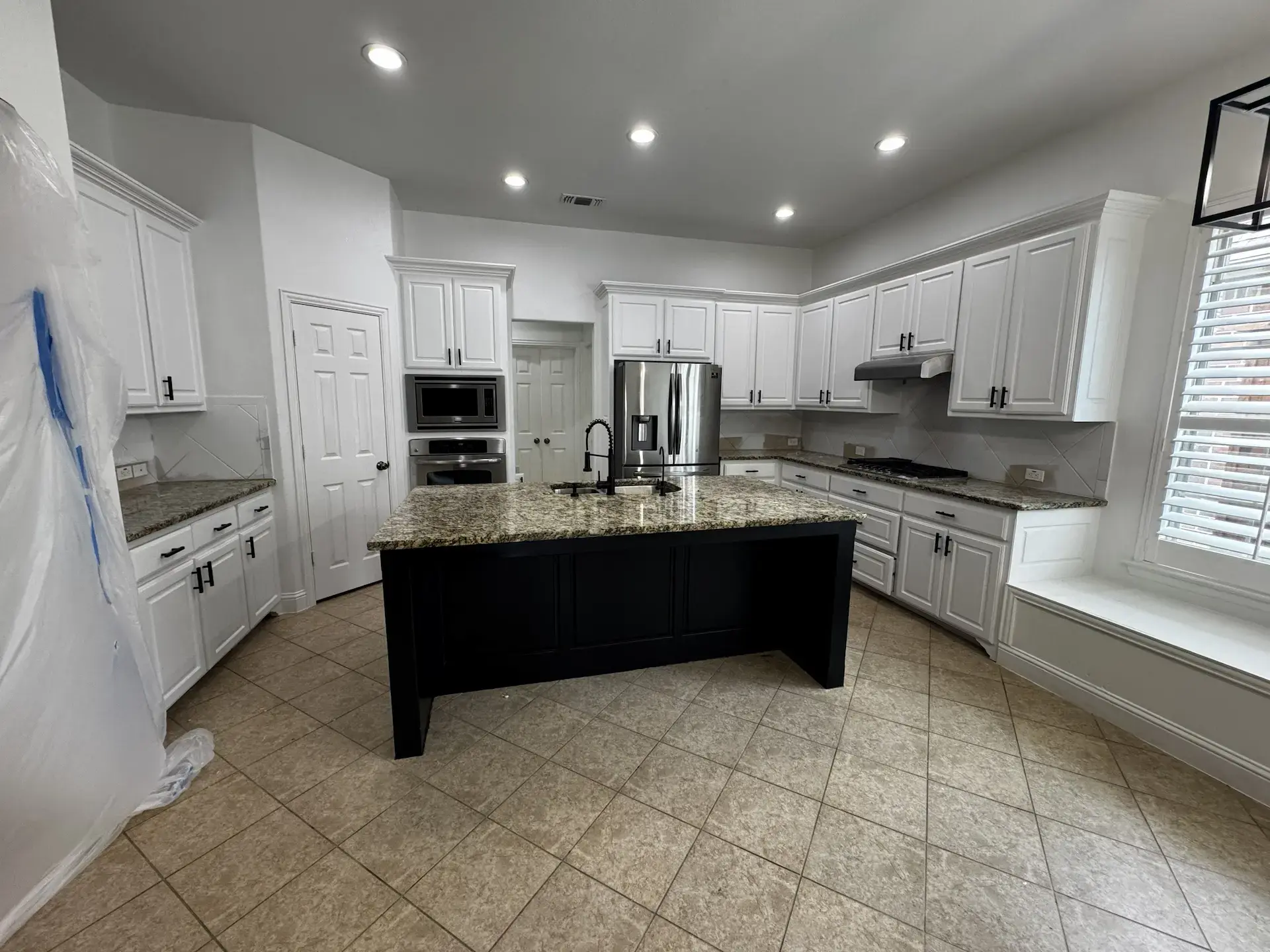 Brightly lit modern kitchen with granite countertops, beautifully painted white cabinets, and a large island with dark painted wood paneling.